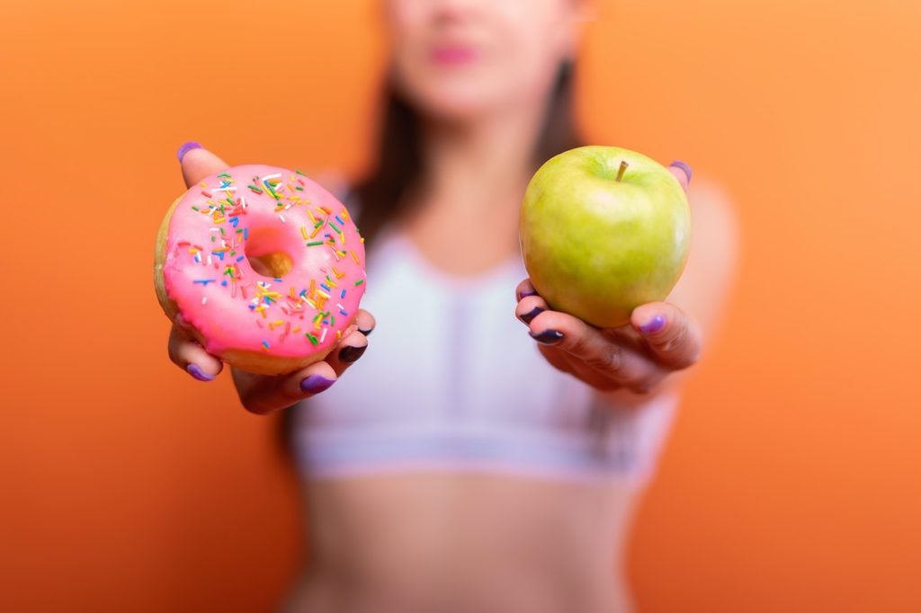 A woman holding an apple and a donut.