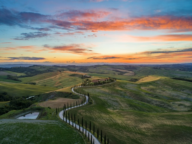 Green fields, a narrow road with cypress trees, sunset in Tuscany