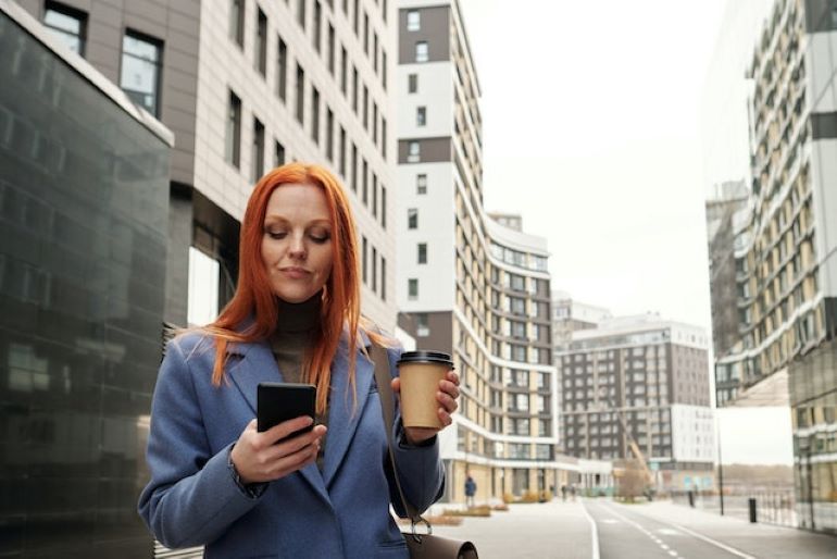 A woman with a cup of coffee and a smartphone in the street. Exploring a new city is one of the ways to deal with homesickness after moving from Italy to New York