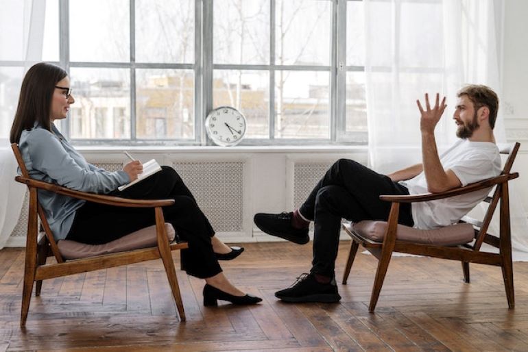 Two people are sitting in a room, talking.